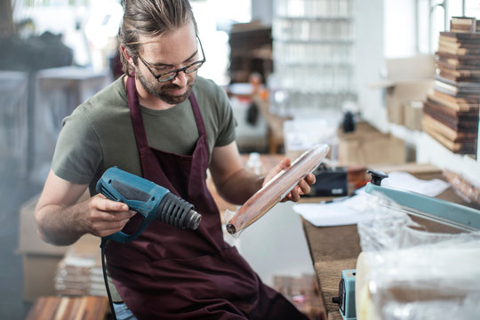 Man heating up plastic wrap on wooden spindle in factory