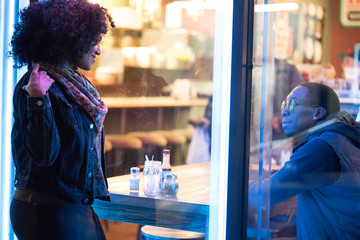 Woman looking through cafe window at friend