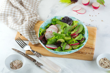 Salad with fresh radishes, arugula, beets, chard, sunflower seeds, flax and sesame seeds on a light background. Selective focus. top view. Copy space.