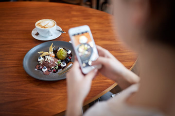 woman with smartphone photographing food at cafe