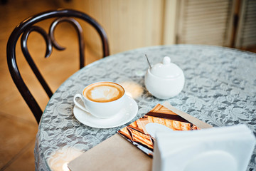 Cup of cappuccino on the table with lace tablecloth. Cozy cafe or restaurant interior.