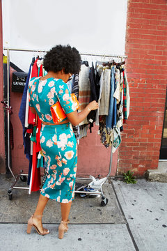 Rear view of young female fashion blogger with afro hair looking at sidewalk clothes rail, New York, USA