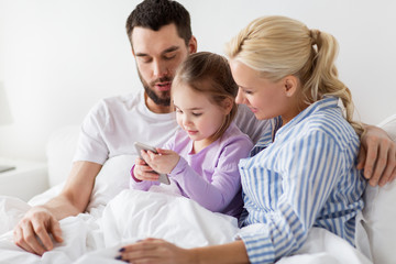 happy family with smartphone in bed at home
