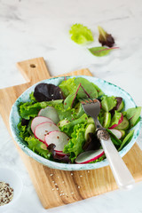 Salad with fresh radishes, arugula, beets, chard, sunflower seeds, flax and sesame seeds on a light background. Selective focus. top view. Copy space.