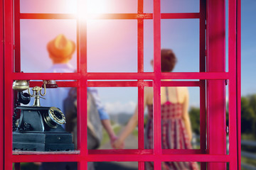 Red vintage phone box in close up view with blur image of Rromantic man and woman