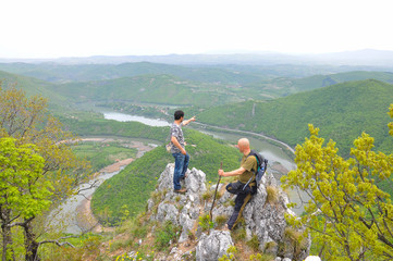 Fototapeta na wymiar Hikers on top of a mountain enjoy the beautiful view of nature, forest and river in valley. View on meanders of Morava river from Kablar, Serbia