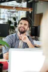 Happy thinking man in office coworking while using laptop