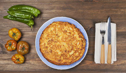 From above typical Spanish omelette with tomatoes, green peppers and oil in bottle on wooden table.