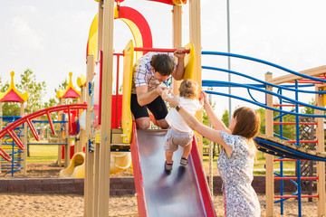 summer, childhood, leisure and family concept - happy child and his parents on children playground climbing frame