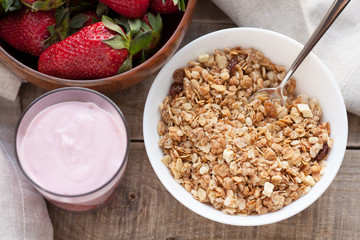 A bowl of homemade granola with yogurt and fresh strawberries on a wooden background. Healthy breakfast