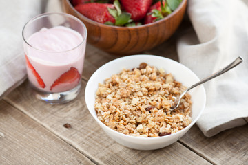 A bowl of homemade granola with yogurt and fresh strawberries on a wooden background. Healthy breakfast