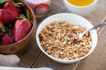 A bowl of homemade granola with yogurt and fresh strawberries on a wooden background. Healthy breakfast with green tea