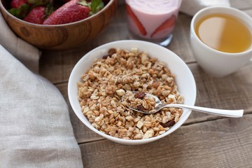 A bowl of homemade granola with yogurt and fresh strawberries on a wooden background. Healthy breakfast with green tea
