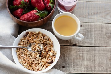 A bowl of homemade granola with yogurt and fresh strawberries on a wooden background. Healthy breakfast with green tea