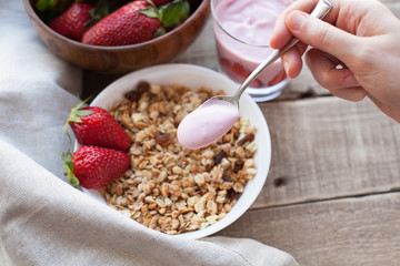 Healthy breakfast. Muesli and yogurt with strawberries. A woman's hand puts a spoonful of yogurt in the muesli