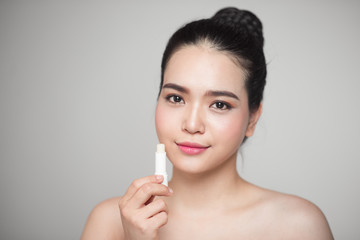 Asian woman applying hygienic lip balm over grey background