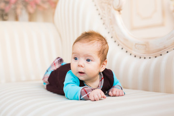 Close-up portrait of baby boy with red hair and blue eyes. Newborn child lyling in couch.