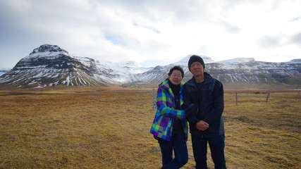 Fototapeta na wymiar Asian senior couple enjoy anniversary trip in Europe. Iceland volcanic landscape mountain with snow view