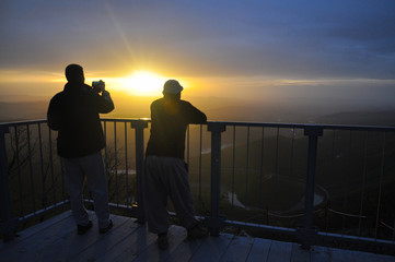 Fototapeta premium Two hikers enjoy in misty morning and sunrise on mountain. Men taking photo with mobile phone on Panoramic view on meanders of Morava river from Kablar, Serbia