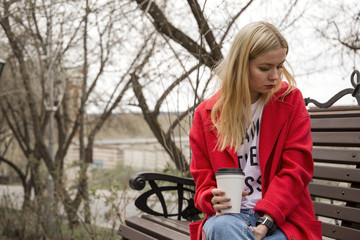 Beautiful girl in red coat drinks coffee to go (space for logo)
