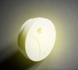 White smoke detector on table with yellow sound emission waves. Smoke detector is a device that senses smoke, typically as an indicator of fire. 