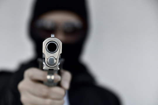 Criminal robber with aiming gun, Bad guy in hood holding pistol handgun.