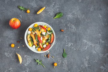 Peach salad. Spinach leaves, arugula, sliced peaches, mango, nuts, feta cheese on black background....