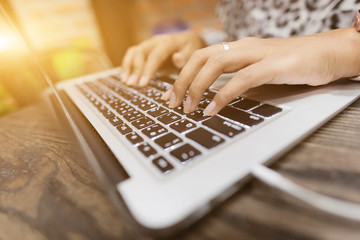 Hands of woman working on the laptop in selective focus with warm fall color.