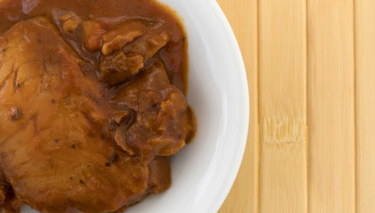 Top close view of a bowl of tilapia fillets in marinara sauce on a wood place mat.