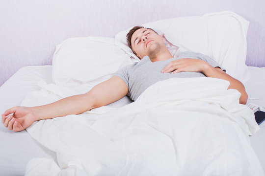 Beautiful, sexy, young man lies in bed with white sheets in the room, sees a good sleep