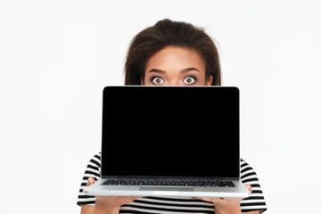 Surprised shocked african woman hiding behind blank screen laptop