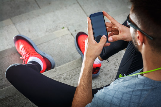 Man relaxing after jogging.He using his smart phone and listening to music.