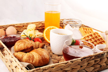 breakfast in bed with fruits and pastries on a tray -waffles, croissants, coffe and juice