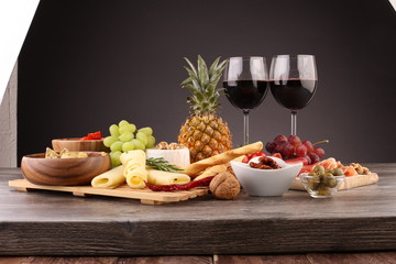 Italian antipasti wine snacks set. Cheese variety, Mediterranean olives, pickles, Prosciutto di Parma with grapes, wine in glasses over black grunge background