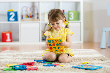Little girl child playing with lots of colorful plastic digits or numbers indoors.