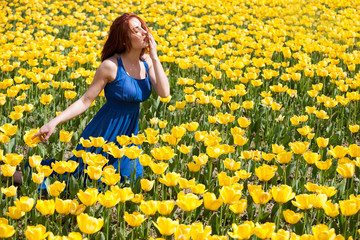 Fototapeta premium Attractive woman in blue dress in beautiful flower field in sunny summer day. Beautiful girl in springtime