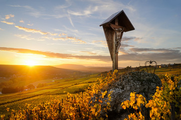 Feldkreuz, Kruzifix im Weinberg mit herbstlicher Laubfärbung bei Sonnenuntergang, zwischen...