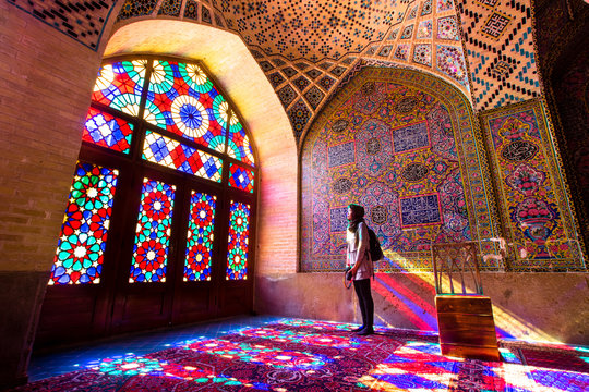 An asian female tourist facing the multicolors light through spectacular stained glass in Nasir Al-Mulk Mosque (Pink Mosque) in Shiraz - Iran.