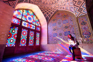 An asian female tourist facing the multicolors light through spectacular stained glass in Nasir Al-Mulk Mosque (Pink Mosque) in Shiraz - Iran.