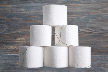 Stack of toilet paper rolls on wooden table against white brick wall. Copy space.