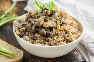  Buckwheat porridge and meat in a white bowl on a wooden table.