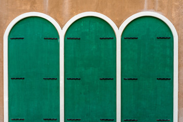 Three green wooden doors on brown concrete wall