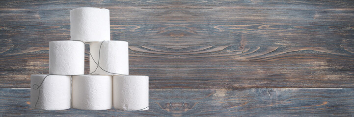 Stack of toilet paper rolls on wooden table against white brick wall. Copy space. Wide panoramic image.