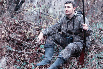 A man in camouflage and with a hunting rifle in a forest on a spring hunt