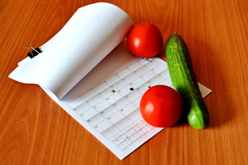 bent sheet monthly calendar with phases of moon, vegetables, tomato and cucumber on wooden table