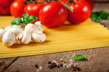 Italian dry pasta spaghetti with tomatoes and fresh herbs on a dark wooden background, selective focus
