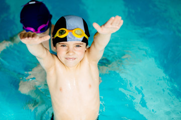 Two little sporty kids workout with hands up in swim pool. Swimming school for small children. Healthy kid enjoying active lifestyle.