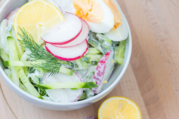 Vegetable salad with yogurt dressing with eggs in a white bowl on wooden board. Various vegetables in a white bowl on wooden board. Healthy summer snack. Clean eating.
