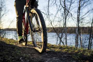 Fototapeta premium Cyclist resting after a ride along the banks of the river, spring evening in the setting sun.