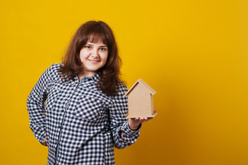 Cute young woman holding a model of house on yellow background.